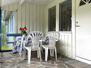 A porch with two white plastic chairs, a table with a blue and white patterned tablecloth, and a vase with red flowers. - 6 Person Holiday Home in Trollhattan (Trollhattan)
