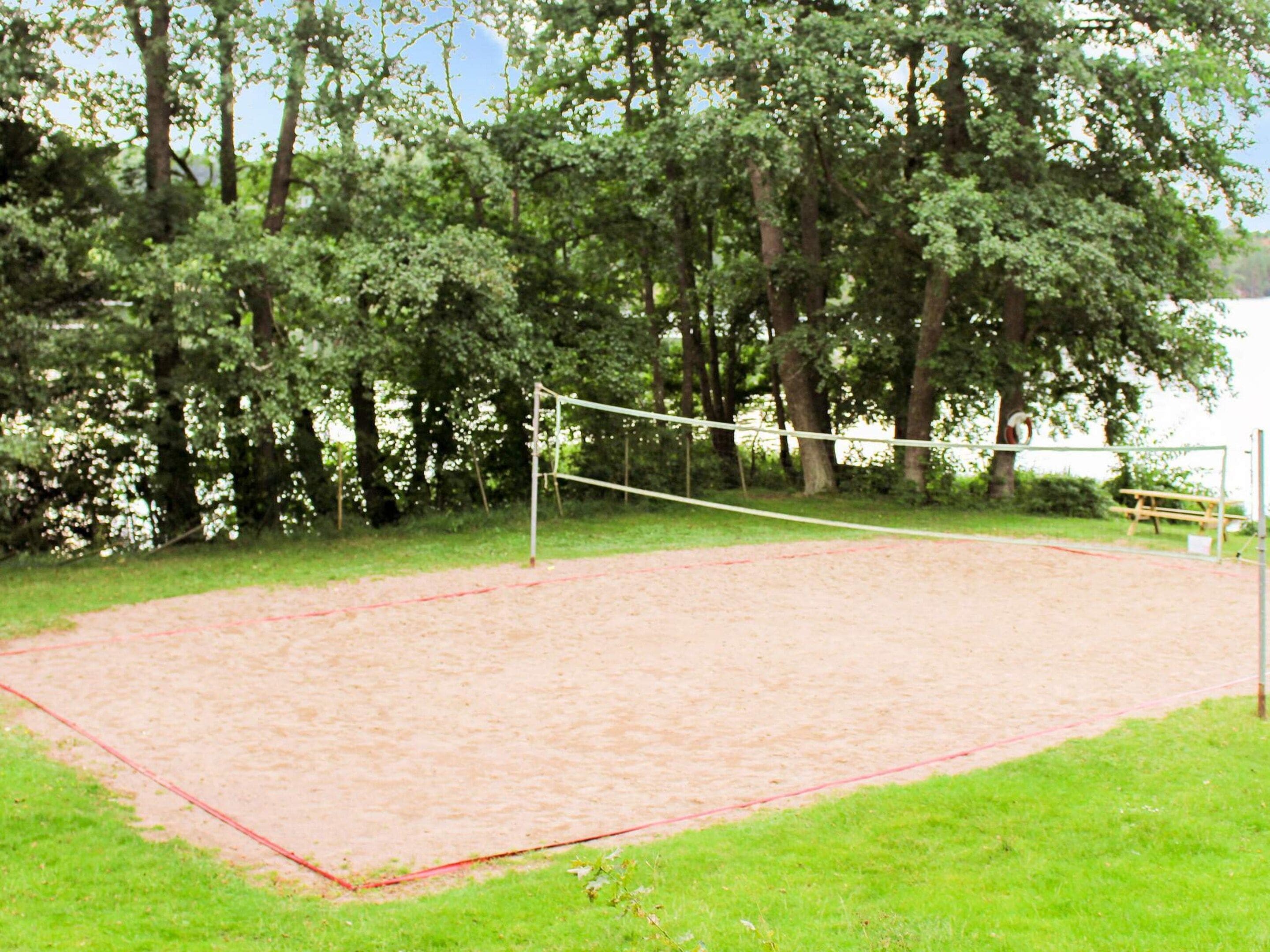 A volleyball court with a net, surrounded by trees and grass.