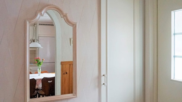 Una habitación con una puerta blanca, un espejo y vistas a un comedor con mesa y sillas.