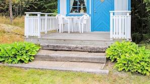Una pequeña cabaña azul con un porche, sillas blancas y una escalera de madera.