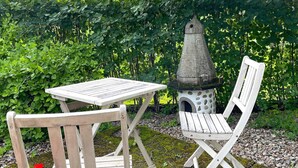 A garden setting with a wooden table and chair, a birdhouse, and red flowers. - 6 Person Holiday Home in Trollhattan (Trollhattan)