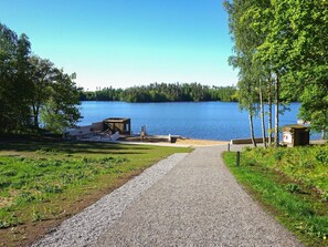 Un chemin de gravier mène à une zone au bord du lac, où se trouvent un quai en bois et une petite cabane.