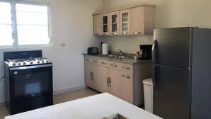 Une cuisine équipée d’une cuisinière à gaz, de placards, d’un réfrigérateur et d’une fenêtre.
