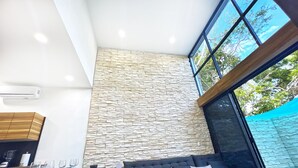A modern living room with a stone wall, a sofa, a coffee table, and a dining area with glasses and bowls.