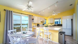 Una cocina luminosa con armarios blancos, una isla central y vista al mar.