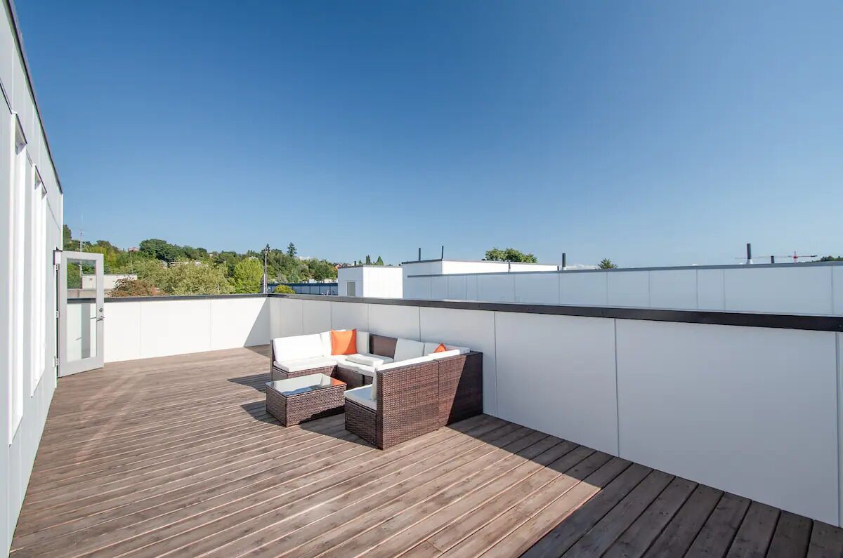 Una terraza en la azotea con piso de madera, paredes blancas y una zona de estar con mobiliario de mimbre.