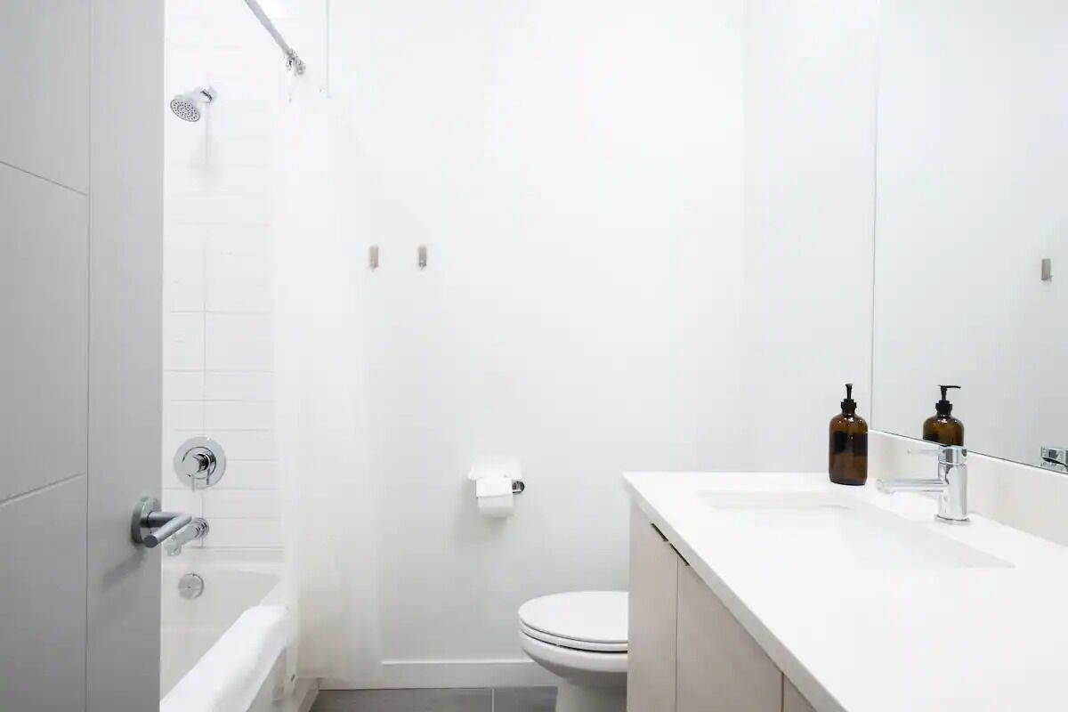 Casa de banho moderna com lavatório branco, espelho e chuveiro.