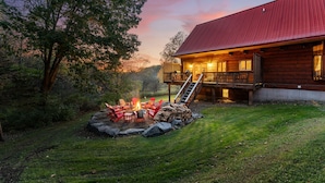 Une cabane en bois avec un toit rouge, une terrasse et un foyer avec des chaises.