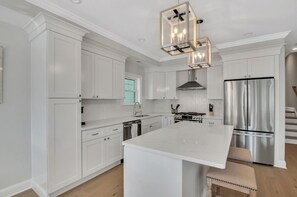 Cocina moderna con armarios blancos, una isla grande, electrodomésticos de acero inoxidable y una lámpara colgante.