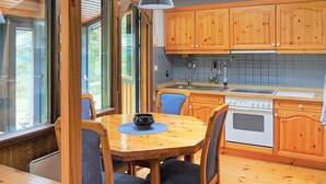 A wooden dining table with chairs, a kitchen with wooden cabinets, a stove, and a window with curtains. - 5 Person Holiday Home in Knared (Knared)