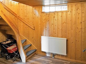 Een houten interieur met een trap, een radiator en een kinderwagen.