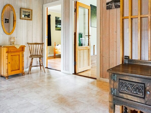 A room with a wooden cabinet, a chair, a wooden door, and a mirror on the wall.