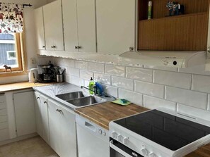 A kitchen with white cabinets, a dishwasher, a stove, and a window with a curtain.