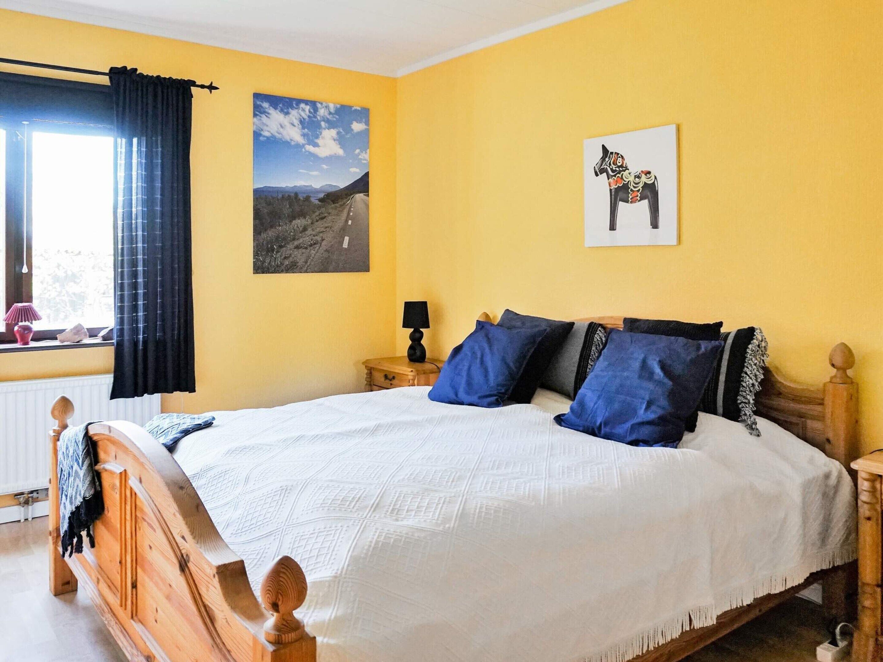 Un dormitorio con una cama de madera, una mesita de noche, una lámpara, una ventana con cortinas y dos obras de arte en la pared.