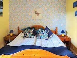 A double bed with floral-patterned pillows, a wooden headboard, and a blue and white quilt. - 8 Person Holiday Home in Lima (Lima)