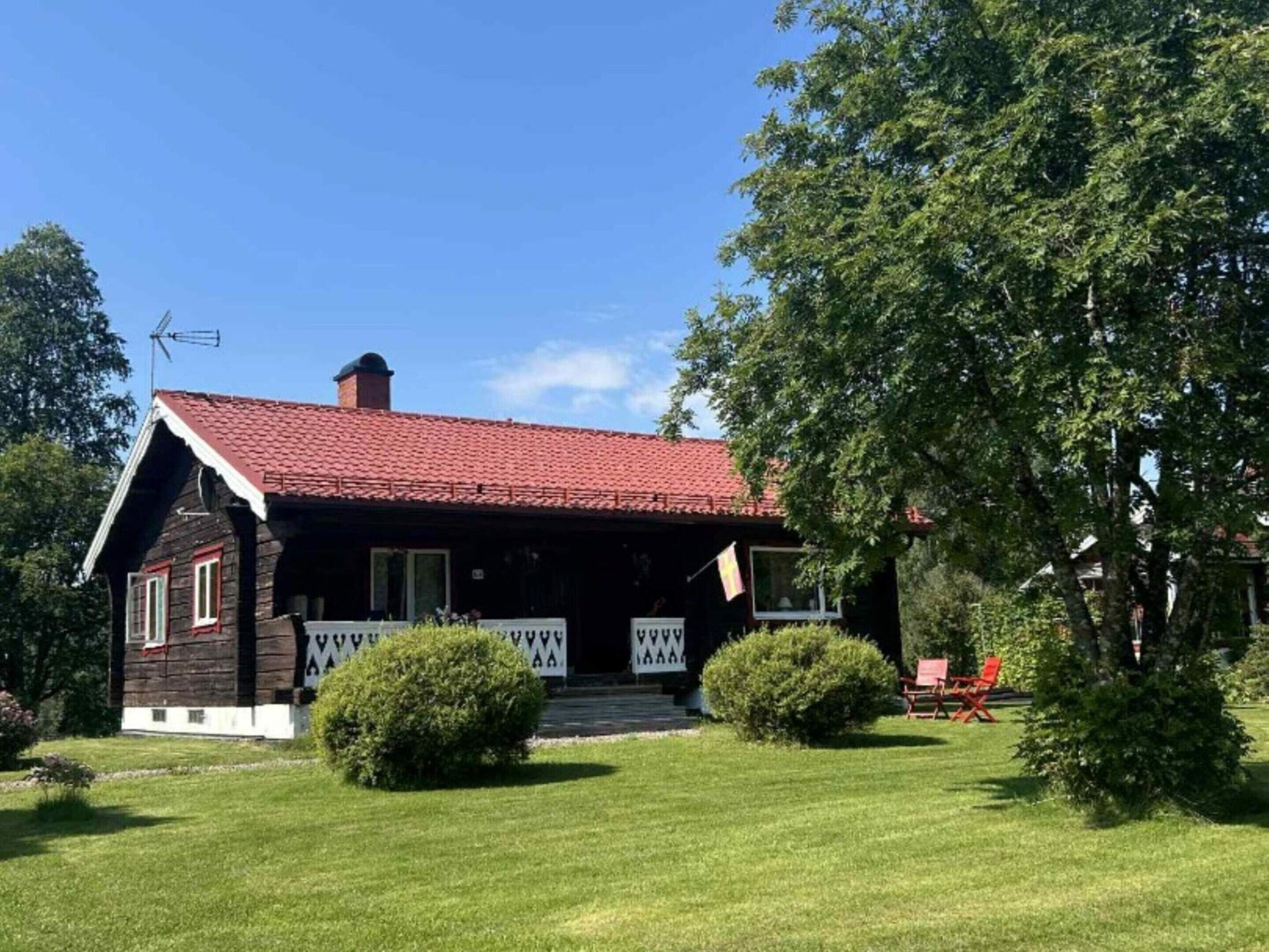 Ett rustikt trähus med ett rött tegeltak, en veranda och en välskött gräsmatta.