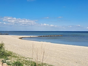 A beach with clear skies, calm water, and a rocky breakwater.