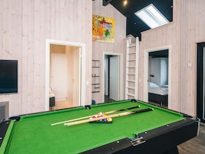 A pool table with balls, a ladder, and a painting on the wall.