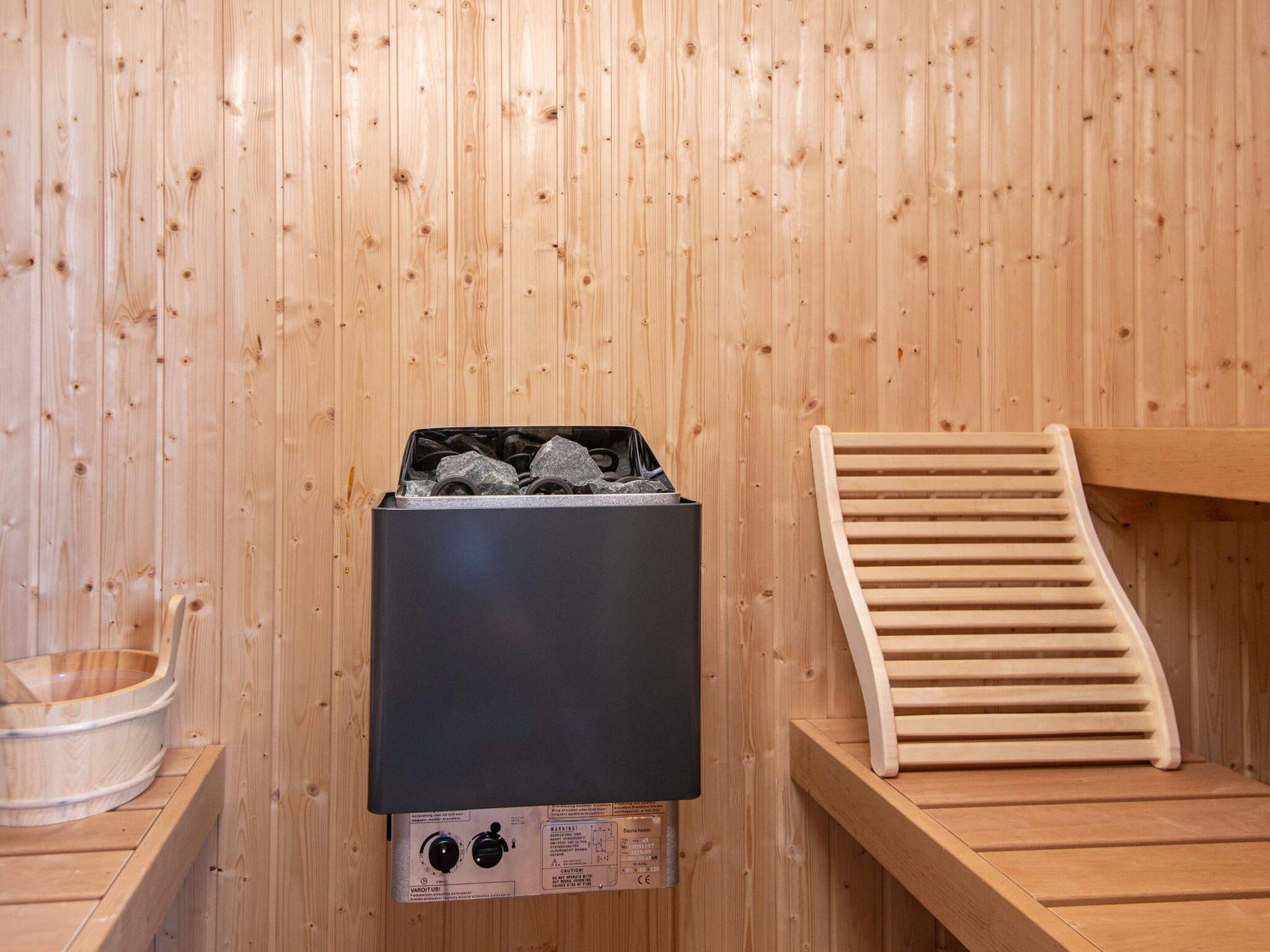 A sauna room with a sauna heater, a wooden bench, and a small wooden table.