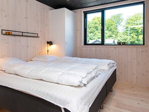 A bedroom with a large bed, a bedside lamp, a window with a view of trees, and wooden paneling on the walls.