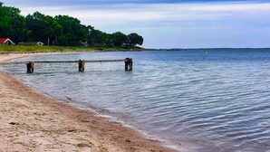 A beach with a wooden pier extending into calm waters, surrounded by greenery and houses. - 5 Star Holiday Home in Haderslev (Haderslev)