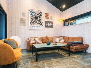 Een moderne woonkamer met een bruine bank, een ronde oranje fauteuil, een bijzettafeltje en een groot abstract schilderij aan de muur.