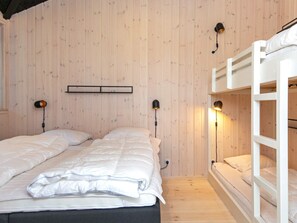 Een kamer met twee bedden, een stapelbed, houten wanden en wandlampen.
