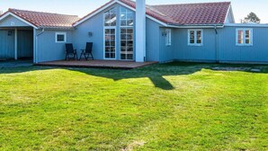 A single-story house with a red-tiled roof, a covered patio with two chairs, and a well-maintained lawn.