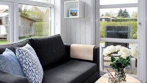 A modern living room with a grey sofa, patterned cushions, a wooden side table, and a vase of white flowers.