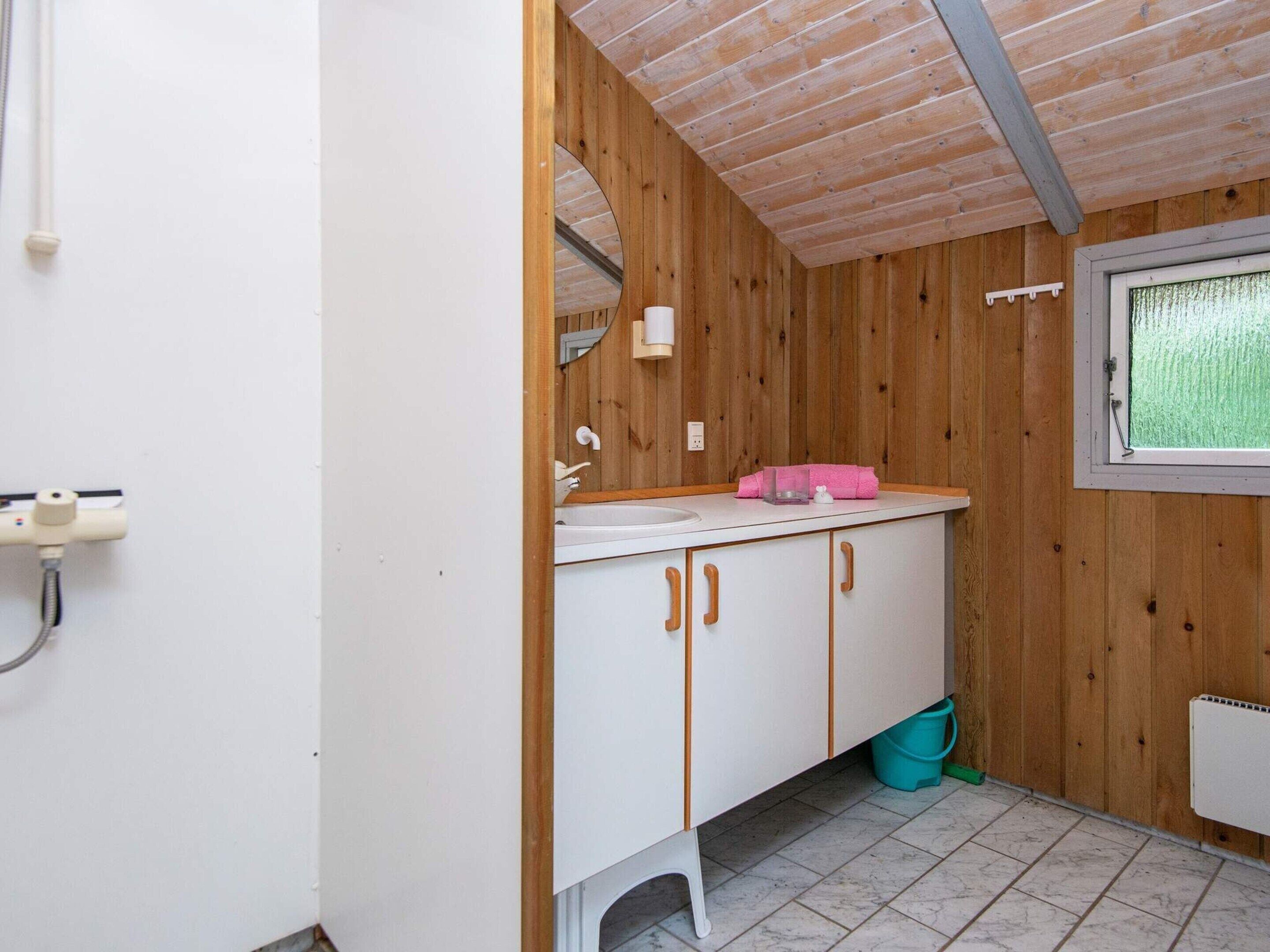 A small, compact bathroom with wooden walls, a white sink, and a window.