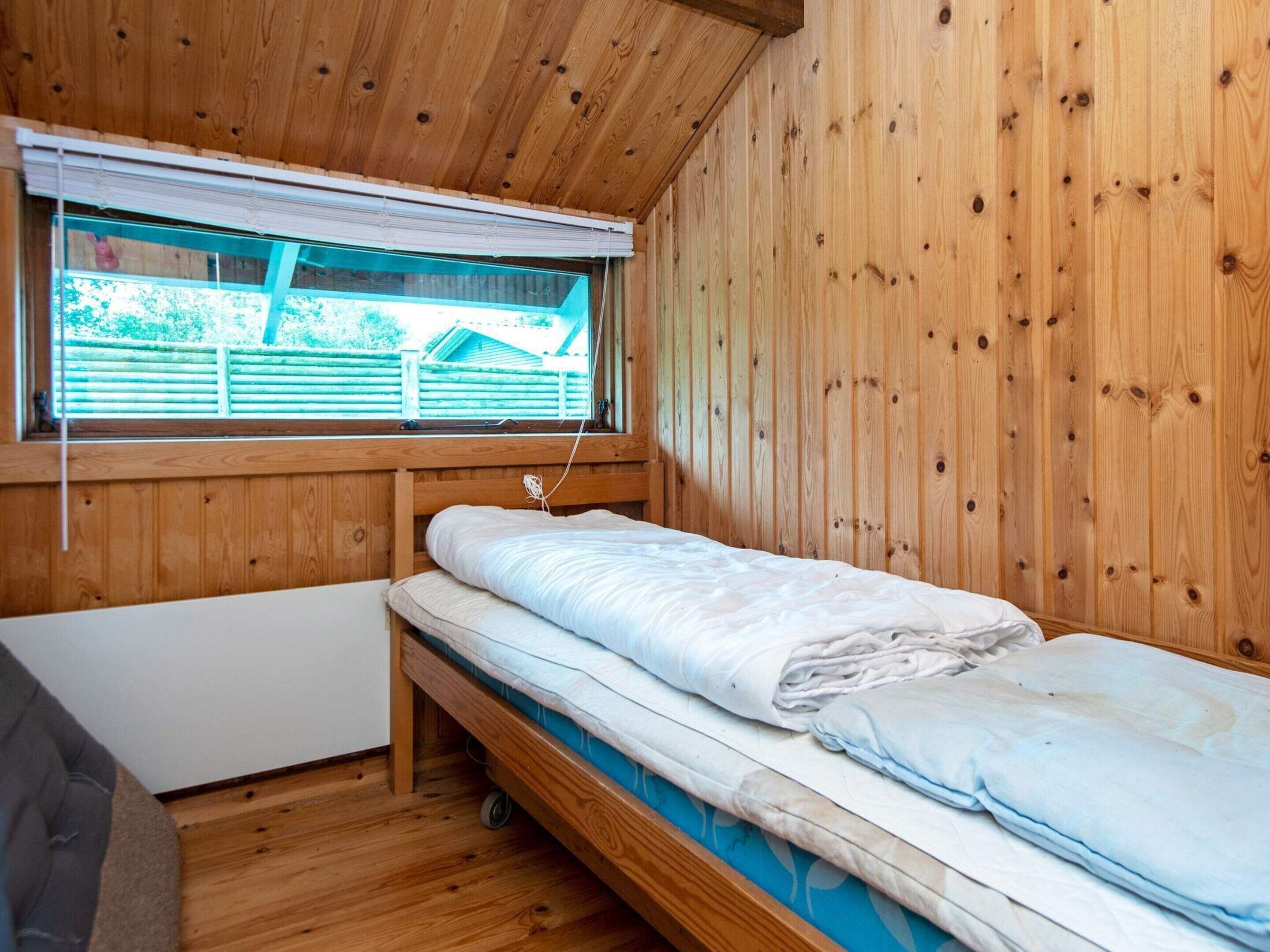 Een kleine kamer met houten lambrisering, een enkel bed, een raam met zonwering en een radiator.