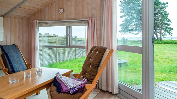 Une cabane en bois avec une table à manger, un fauteuil rembourré et une vue sur un espace verdoyant par une grande fenêtre.