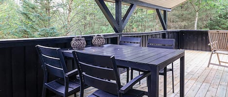 An outdoor wooden deck with a table and chairs, surrounded by a wooden fence, and overlooking a wooded area.