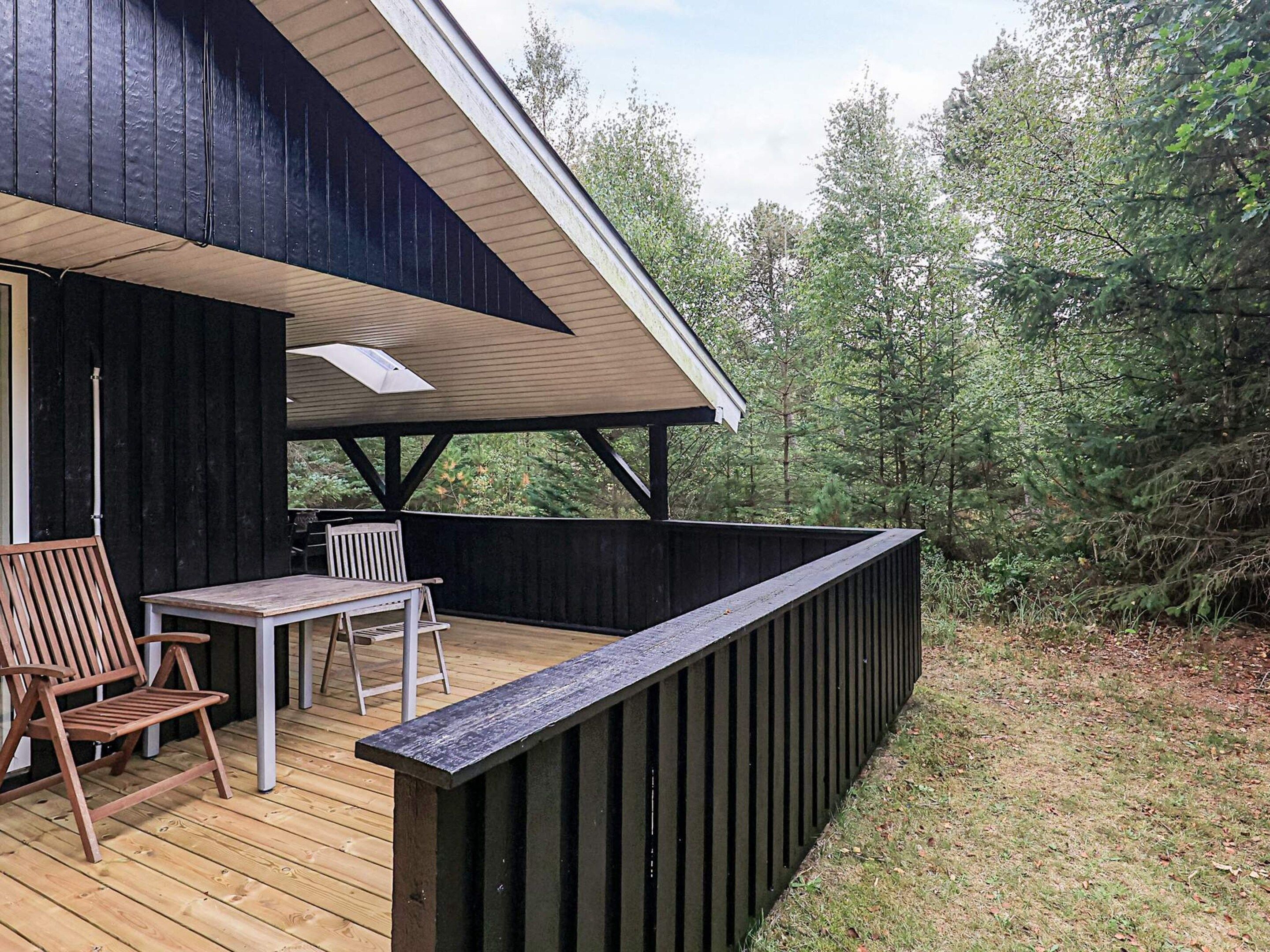 A wooden deck with a table and chairs, a covered area, and a view of trees.