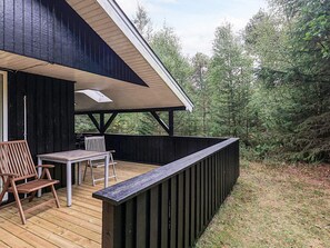 Une terrasse en bois avec une table et des chaises, un espace abrité et une vue sur les arbres.