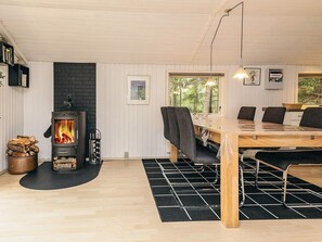 Una habitación acogedora con una estufa de leña, una mesa de comedor con sillas y un gran ventanal con vistas al exterior.