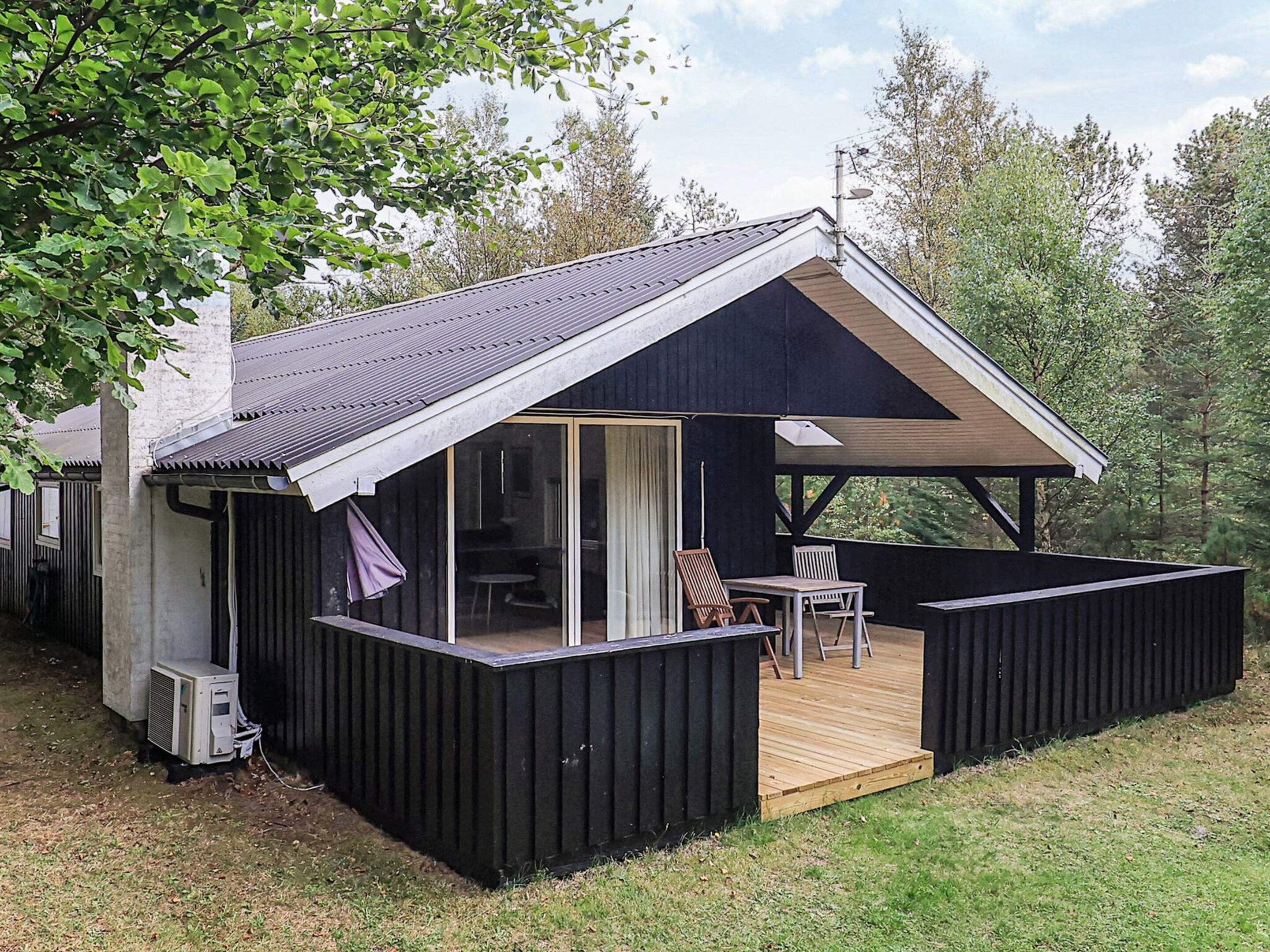 A cabin with a covered deck, a sliding glass door, and a patio area with outdoor furniture.