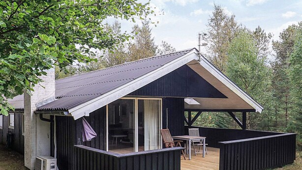 Une cabane dotée d’une terrasse couverte, d’une porte-fenêtre coulissante et d’un espace patio aménagé avec du mobilier d’extérieur.