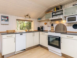 Une cuisine moderne avec des armoires blanches, un four encastré, un four à micro-ondes et une fenêtre donnant sur les arbres.