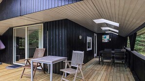 Une terrasse en bois avec une table et des chaises, une porte vitrée et un tableau d’affichage.