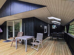Une terrasse en bois avec une table et des chaises, une porte vitrée et un tableau d’affichage.