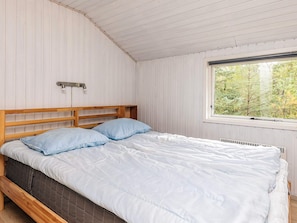 A bedroom with a wooden bed frame, white bedding, and a window with a view of trees.