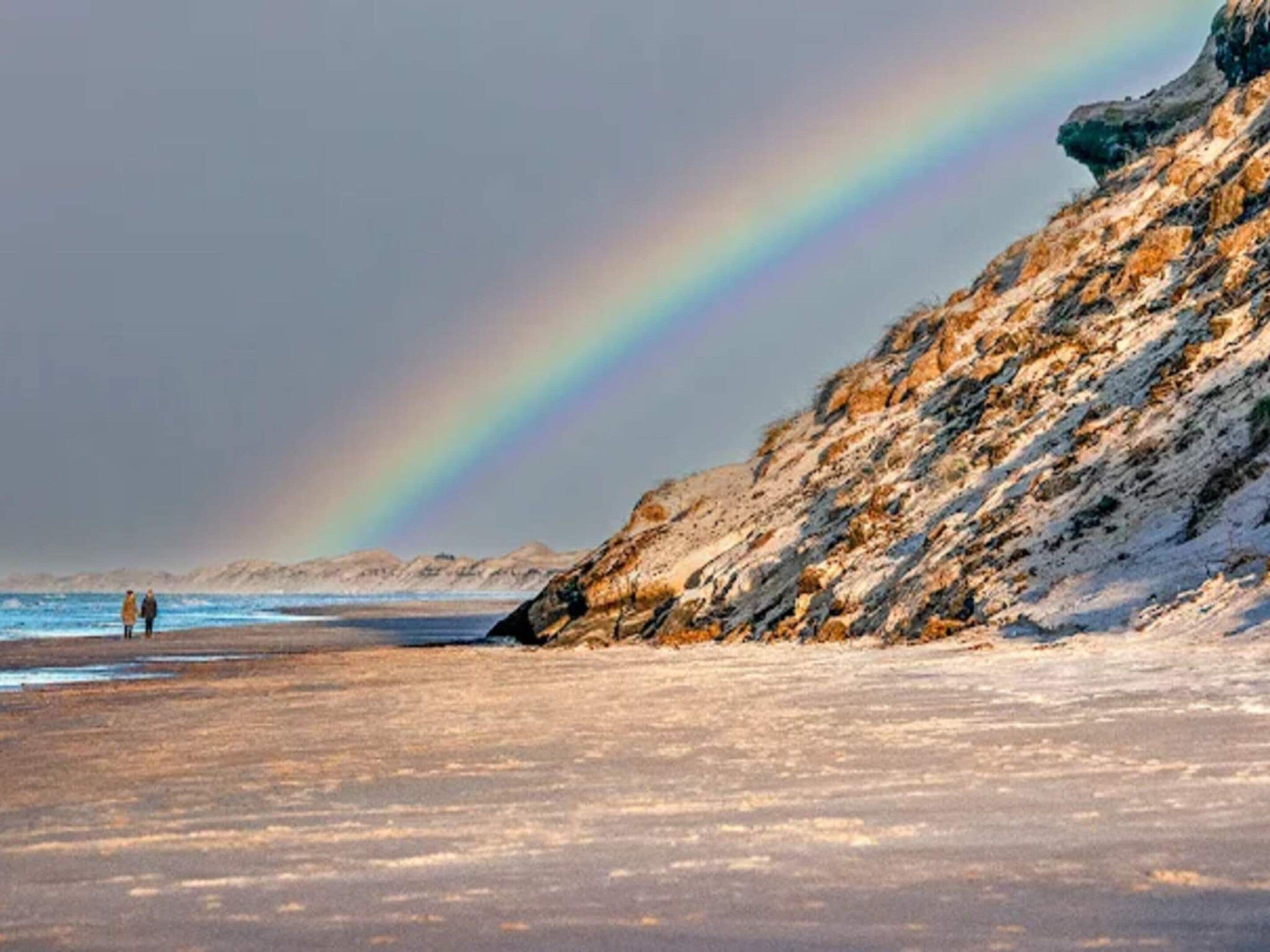 Une plage avec un arc-en-ciel et des falaises rocheuses.