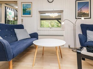 A room with a blue sofa, a white table, a floor lamp, and a window with a view of trees. - 5 Person Holiday Home in Albaek (Aalbaek)