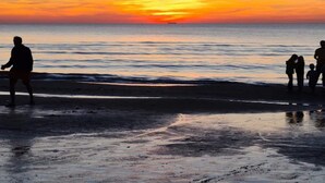 Une scène de plage où l’on aperçoit des silhouettes de personnes se détachant sur le ciel d’un coucher de soleil.