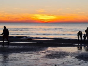 Une scène de plage où l’on aperçoit des silhouettes de personnes se détachant sur le ciel d’un coucher de soleil.