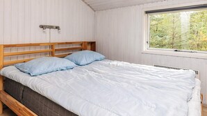 Une chambre avec un lit en bois, des murs blancs, une fenêtre donnant sur des arbres et un plafond avec des poutres en bois.
