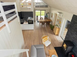 A modern interior with a loft bedroom, a kitchen, a dining area, and a fireplace. - 5 Star Holiday Home in Lokken (Lokken)