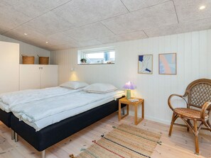 A bedroom with a bed, bedside lamp, chair, and a small window. - 5 Star Holiday Home in Lokken (Lokken)