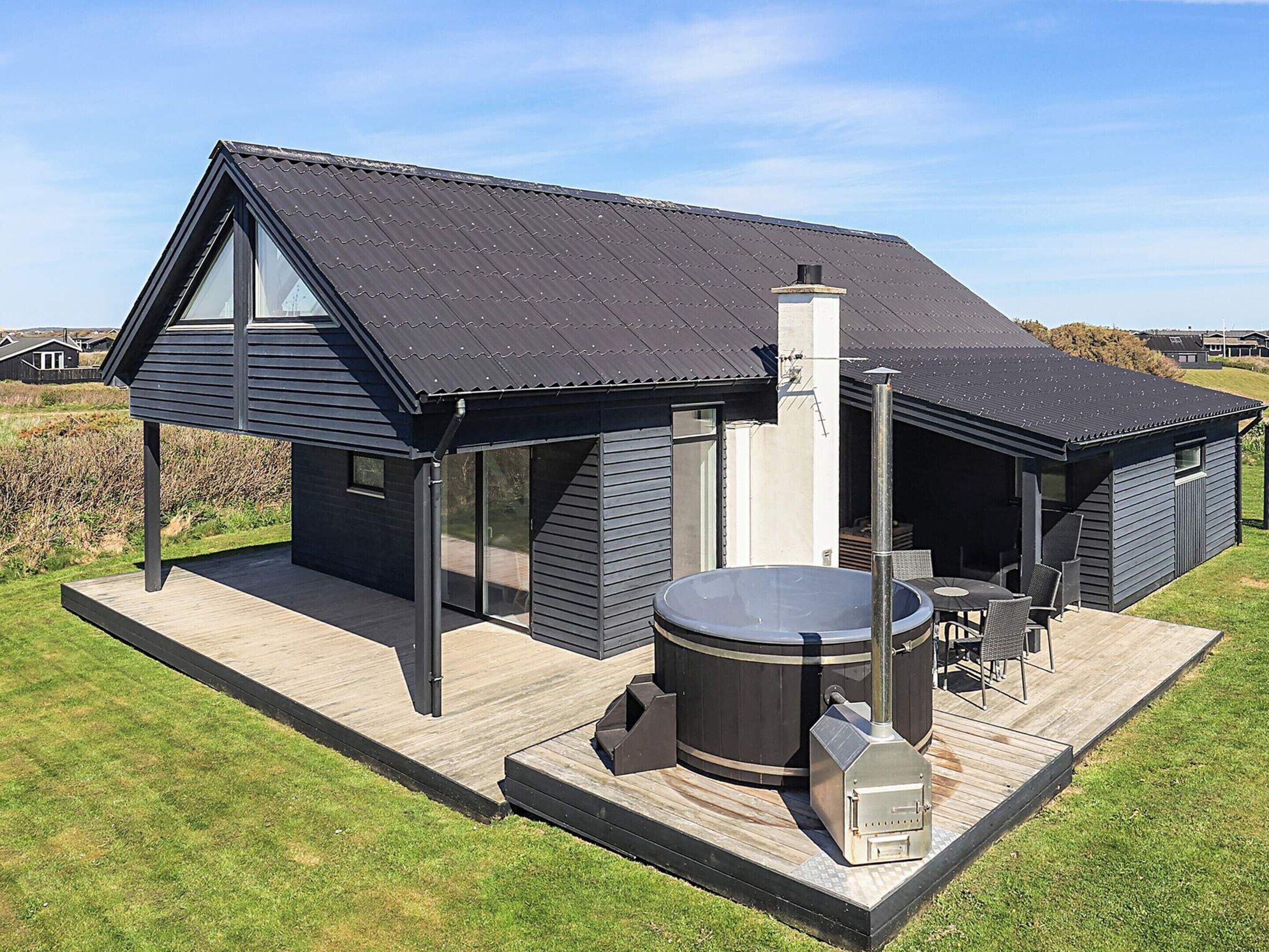 A modern house with a hot tub, outdoor seating, and a chimney.